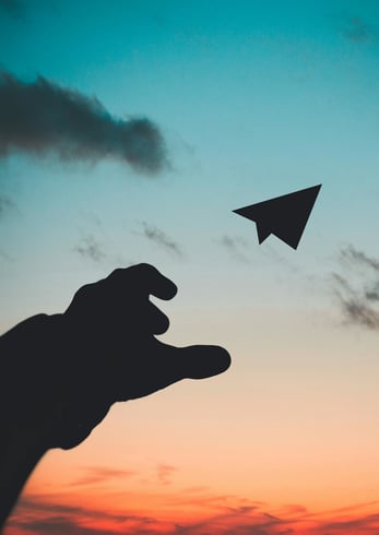 backlit-shaded-hand-throwing-paper-plane-into-dusk-sky backlit-shaded-hand-throwing-paper-plane-into-dusk-sky