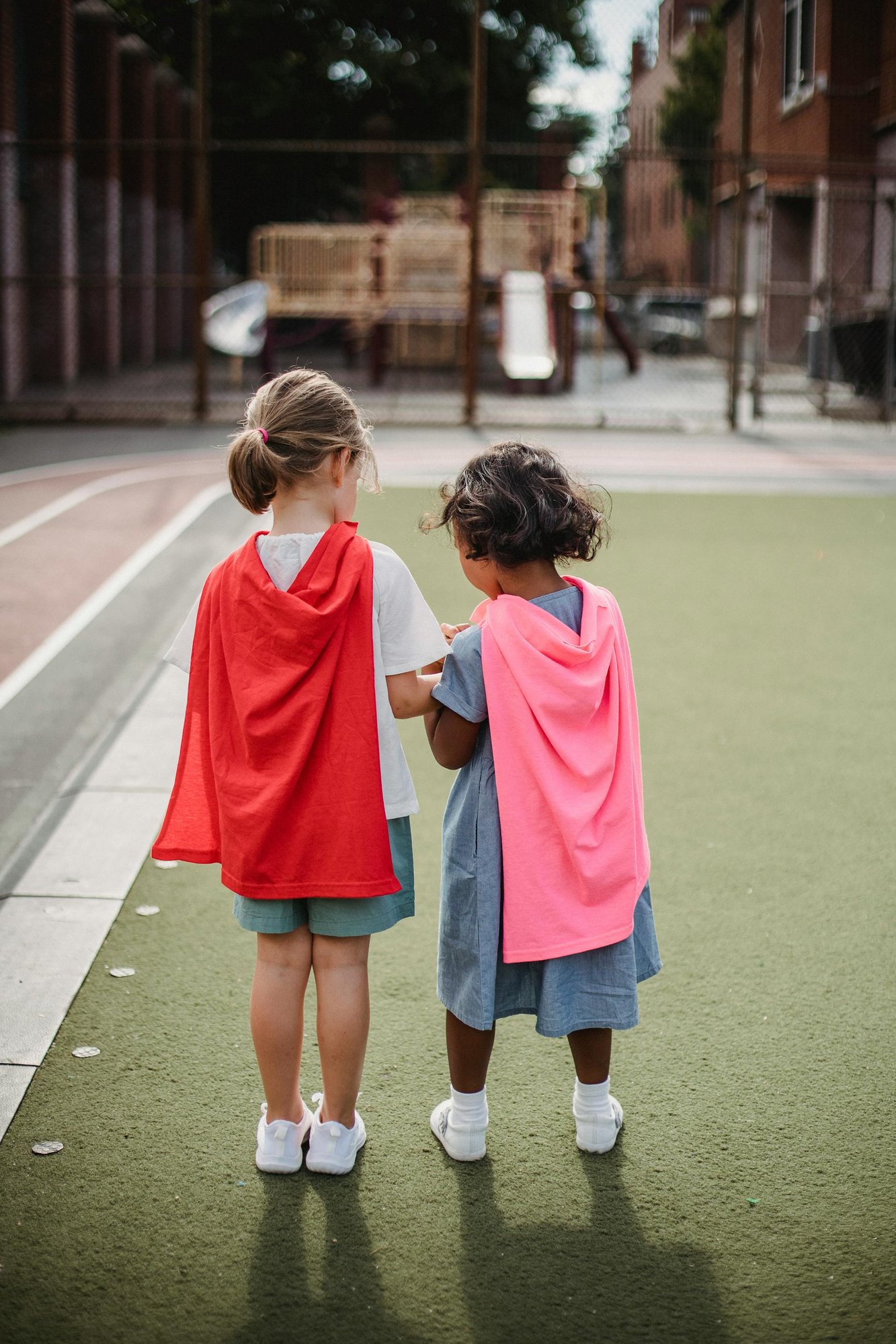 Two children wearing capes on a playground.